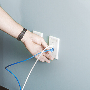 Une personne branche un câble réseau dans une prise au mur